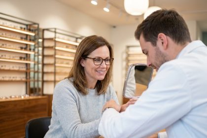 Femme en consultation chez l'opticien essayant des lunettes rectangulaires dans une boutique moderne